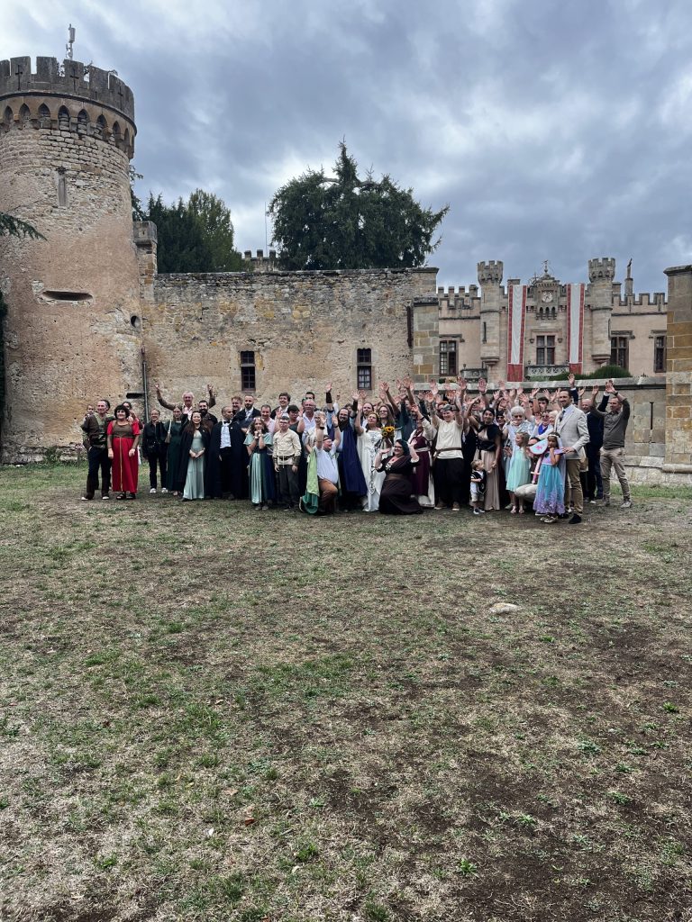 Les mariés et leurs invités en costumes médiévaux lèvent les bras dans la cour du Château de la Grange Fort
